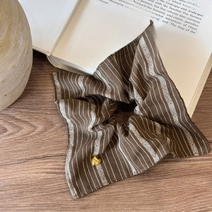 Close-up of vintage brown striped scrunchie with a gold heart pendant on a book