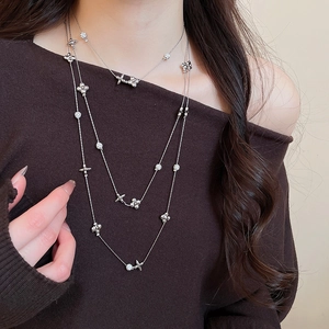 Close-up of layered silver necklace with floral and cross charms on brown sweater