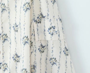 Detailed close-up of blue floral print on white chiffon dress with pocket and button