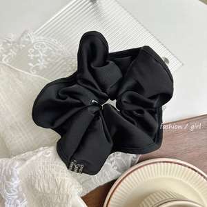 Détail du chouchou géant en satin noir avec plis multicouches et étiquette faite main