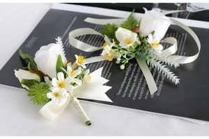 Detailed close-up of two white silk rose boutonnieres with green leaves and cream ribbons