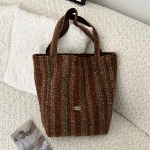 Detail of a brown shearling tote bag featuring dark vertical stripes and a gold logo plate