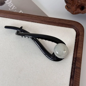 Detail of a black twisted hair claw clip with a large translucent cream bead decoration