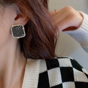 Close-up of a square houndstooth stud earring with white rhinestones on a female model