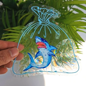 Detailed holographic suncatcher sticker featuring a shark design held against green leaves
