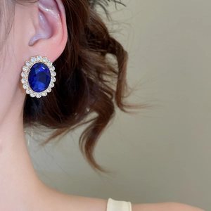 Close-up of royal blue oval sapphire earring with surrounding white diamonds on model