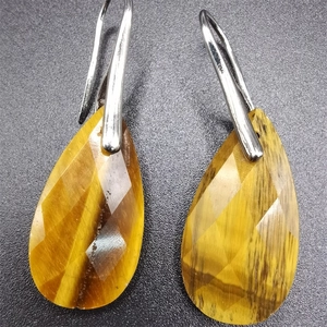 Macro shot of faceted teardrop-shaped tiger eye earrings with silver hooks on black surface