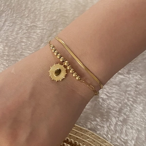 Double-layered gold bracelet with tiger eye sun pendant on soft white fabric