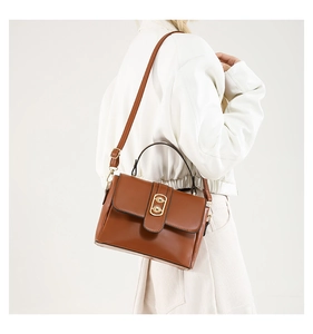 Detail view of a brown leather crossbody bag featuring a gold oval clasp on a model