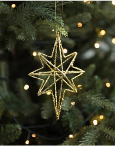 Close-up of a golden glittered star ornament hanging on a green Christmas tree with bokeh