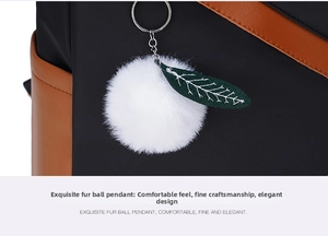 Detail of soft white fur pompom keychain and green leaf charm on black nylon backpack
