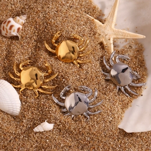Minimalist crab stud earrings in gold and silver finish on sand with starfish