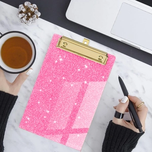 Pink glitter acrylic clipboard with a gold metal clip on white marble desk background