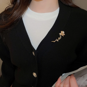 Close-up of elegant gold flower brooch with white pearl on black cardigan