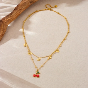 Double-layer gold necklace with red cherry pendants on a natural beige background