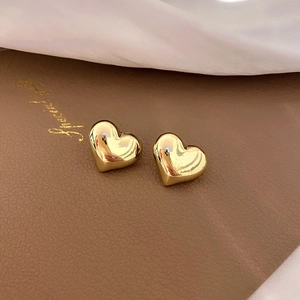 Macro shot of polished gold heart stud earrings on textured brown leather background