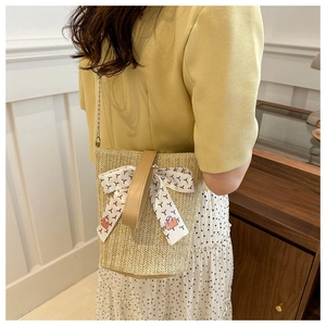 Détail du sac seau en paille avec nœud en foulard et chaîne dorée élégante