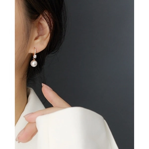 Elegant model wearing gold earring with shimmering crystals and a white pearl drop
