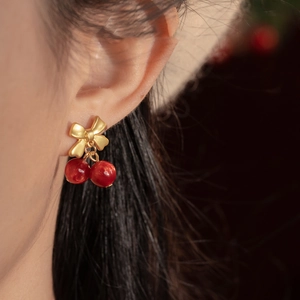 Close-up of cherry bow earrings featuring golden metal bows and vibrant red cherry beads