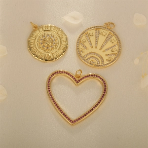 Gold plated zodiac sun and heart pendants with zircon stones on beige background