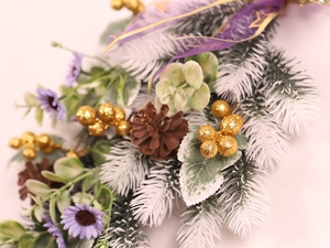 Detail of purple artificial flowers, gold glitter balls, and frosted pine needles with pinecones
