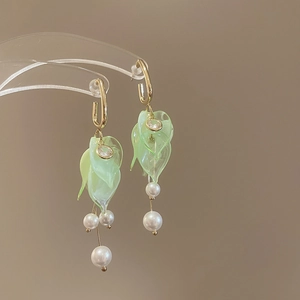 Detail of green acrylic petals and white pearl tassels on elegant gold drop earrings