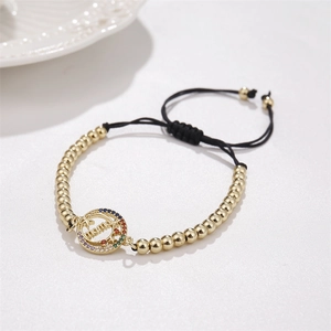 Detail of gold MAMA charm bracelet with colorful cubic zirconia and black cord