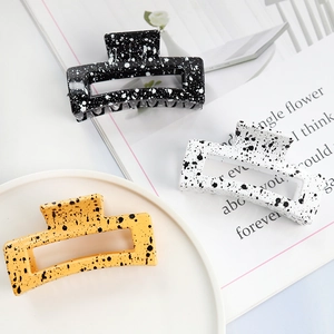 Three square hair claws in black, white, and yellow with ink splash pattern flat lay