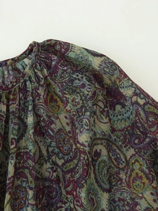 Detailed close-up of paisley print chiffon fabric with golden threads and ruffled neckline