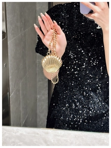Macro shot of shell-shaped golden evening bag with metallic texture and beaded chain