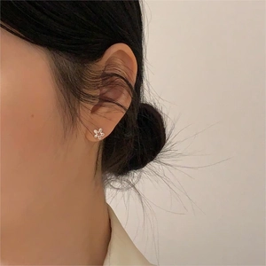 Close-up of minimalist 925 sterling silver flower stud earrings on a model's ear