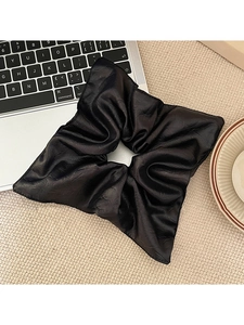 Macro shot of large black pleated square hair scrunchie on a beige textured table