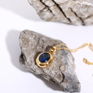 Detail of 18k gold plated necklace with oval blue gemstone on natural grey stones