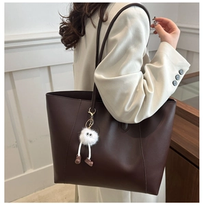 Détail d'un grand sac cabas marron foncé mat avec un petit pendentif monstre en peluche blanc