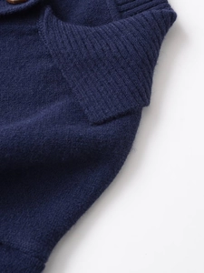 Detail eines dunkelblauen Strickpolos mit geripptem Kragen und hochwertigem braunem Knopf