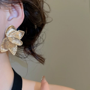 Close-up of golden petal-shaped textured earrings worn by a model in a high-fashion style
