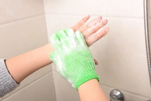 Close-up of green five-finger exfoliating glove creating rich foam on arm in bathroom