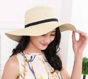 Detail of hand-woven beige straw hat featuring black grosgrain ribbon and wavy brim