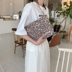 Détail d'une trousse de toilette en velours côtelé violet à fleurs tenue dans un café
