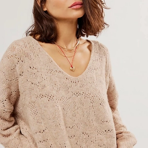 Detail eines Herzanhängers an einer roten Kordel mit goldener Halskette auf Strickware