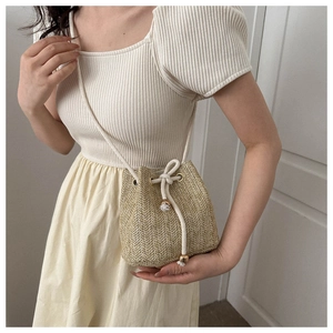 Detail of a handmade straw bucket bag with drawstring closure shown on a model