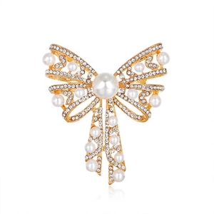 Detail of a golden bow brooch with white faux pearls and crystals on white background