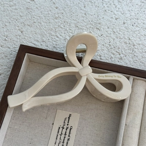 Detail view of beige glossy ribbon hair claw clip with golden text in jewelry box