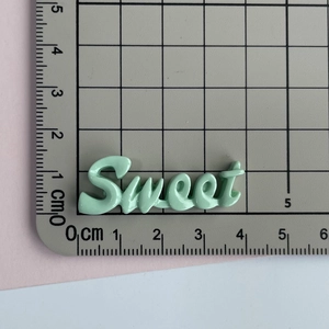 Détail d'un charm Sweet en résine vert clair de 4,5 cm sur un tapis de mesure gradué