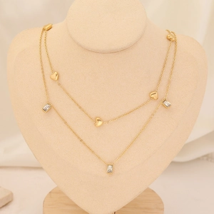 Detail of layered gold heart necklace with square zircon charms on a beige bust display