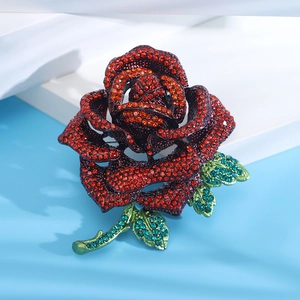 Macro detail of luxury rose brooch featuring red rhinestones and green crystal leaves