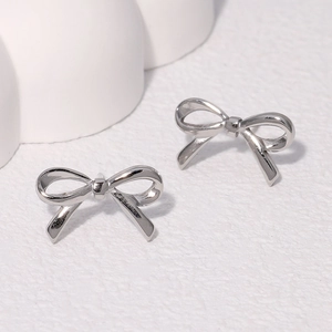 Minimalist polished silver bow knot stud earrings on a clean white textured background