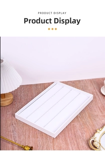 Close-up of a white 4-tier jewelry display tray for rings and earrings on a desk