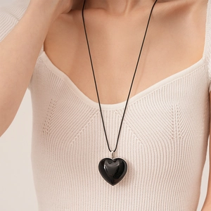 Detail of a black heart pendant with silver edges on a white sweater background