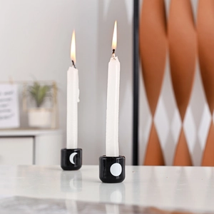 Close-up of black ceramic candle holders with sun and moon prints and lit candles